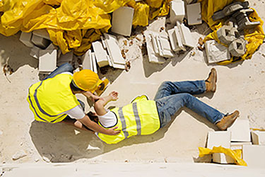 construction worker laying on ground while another working kneels over him