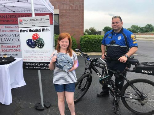police officer standing next to bike with a girl holding a new helmet beside him