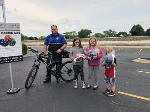 Police officer next to bike beside three kids with new helmets
