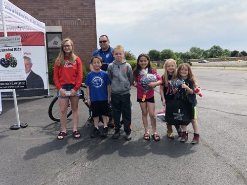 Six children with helmets standing in front of police officer with bike