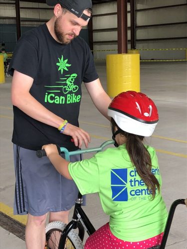 volunteer helping a child wearing a helmet on a bike